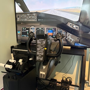 Puede incluir: Una configuración de simulador de vuelo con una pantalla que muestra una escena de pista. La configuración incluye un yugo negro, controles del acelerador y paneles de instrumentos. El yugo tiene un mango negro y un botón amarillo. El simulador está montado en un soporte negro.