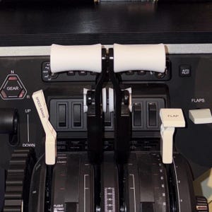 May include: An aircraft cockpit control panel with black levers and white handles. The panel includes labeled controls and switches. The text "SPEED BRAKE" and "FLAP" are visible. The image depicts an aviation theme.