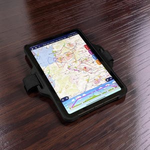Może przedstawiać: Czarny tablet z wyświetloną na ekranie szczegółową mapą, zabezpieczony w czarnym etui z regulowanym paskiem. Ekran pokazuje mapę z różnymi znacznikami i wizualizacjami danych. Urządzenie spoczywa na ciemnej drewnianej powierzchni.