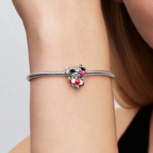 May include: A silver charm bracelet with a detailed charm of a cartoon character wearing sunglasses and a red and white life preserver. The charm is a small, three-dimensional figure with black, pink, and red accents.