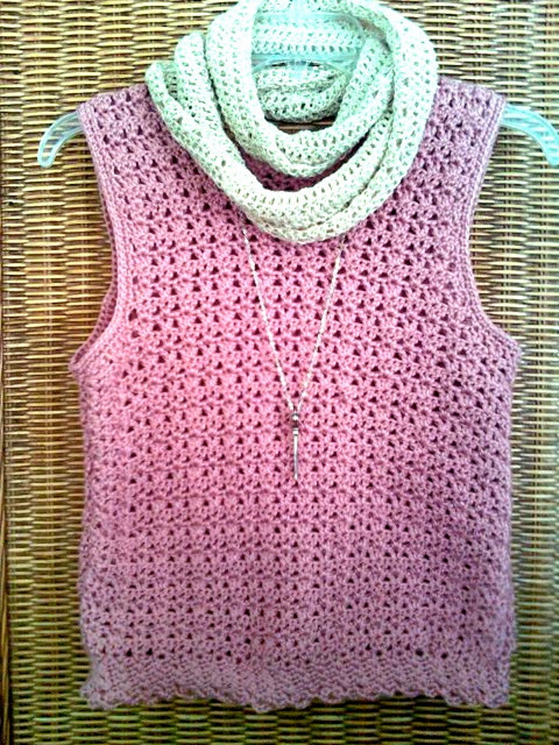 May include: A sleeveless, dusky pink crochet top with a matching crochet scarf and a silver pendant necklace. The top is displayed on a clear hanger. The scarf is a light beige colour. The crochet pattern is visible.