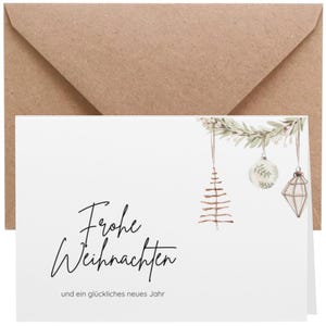 May include: A white Christmas card with the words "Frohe Weihnachten" and "und ein glückliches neues Jahr" in black script. The card features watercolor illustrations of Christmas ornaments and a brown envelope.