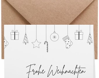 Könnte beinhalten: Eine weiße Weihnachtskarte mit schwarzen Strichzeichnungen von hängenden Ornamenten und Geschenken. Der Text "Frohe Weihnachten" ist in Schreibschrift geschrieben, darunter steht "und ein glückliches neues Jahr". Ein brauner Umschlag befindet sich hinter der Karte.