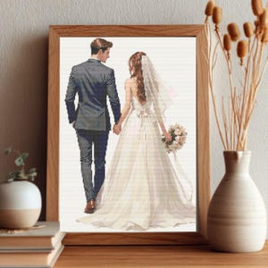 Puede incluir: Impresión enmarcada que muestra a una pareja de espaldas, tomados de la mano. El hombre lleva un traje gris, la mujer un vestido de novia blanco con velo y un ramo. El marco es de madera.
