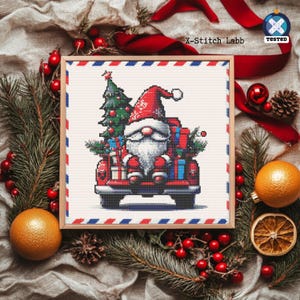 May include: A framed cross-stitch depicting Santa Claus in a red truck laden with presents and a Christmas tree. The image has a festive theme, with the text "X-Stitch Labb" in the upper left corner.