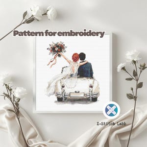 May include: Cross-stitch pattern featuring a bride and groom in a vintage car, with the text "Pattern for embroidery." The bride holds a bouquet. The image is framed in white, with white flowers and fabric in the background.