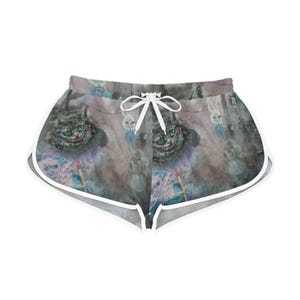 May include: Gray and white shorts featuring a whimsical illustration of the Cheshire Cat from Alice in Wonderland. The shorts have a white drawstring and trim, with a colorful, fantasy-themed design. The shorts are perfect for casual wear.