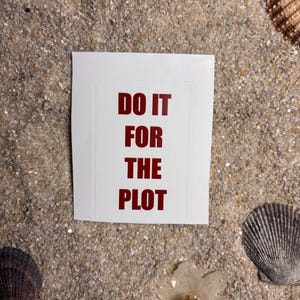Peut inclure: Un autocollant blanc avec le texte "DO IT FOR THE PLOT" en rouge, sur un fond sablonneux avec des coquillages et des fleurs séchées.