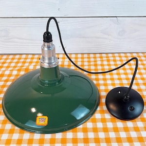 May include: A green enamel pendant light fixture with a black cord and a black ceiling plate. The light fixture has a white porcelain socket and a yellow sticker that reads "Benjamin Electric Mfg. Co.  Made in USA 120V".