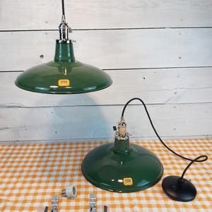 May include: Two green pendant lights with a shiny finish are displayed. One is hanging, and the other is on a table. The lights have a classic industrial design with a black cord and chrome accents. Various hardware components are also visible.