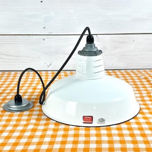 May include: White pendant light with a black cord and a silver-colored base. The light fixture has a rounded shade and a gray top. The light is on a yellow and white checkered tablecloth.