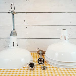 May include: Two white enamel pendant light fixtures with silver hardware. One is assembled, the other is disassembled. The lights are on a yellow and white checkered surface, with a white wooden background.