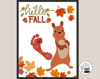 May include: A framed print with a white background featuring a cartoon squirrel, a red footprint, and fall leaves. The text "hello FALL" is written in green and brown. The print is surrounded by a black frame.