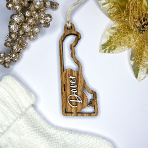 May include: Wooden ornament shaped like the state of Delaware with the word "Dover" written on it in white lettering.