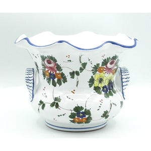 May include: A white ceramic planter with a scalloped rim and two side handles featuring blue striped detailing. The exterior is decorated with hand-painted floral motifs in shades of red, yellow, orange, and green, set against a glossy white finish.