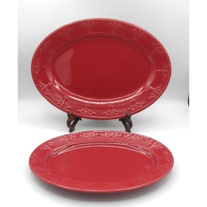 May include: Two oval-shaped red ceramic serving platters with a glossy finish. Each platter features a raised, embossed decorative border pattern along the rim, consisting of repeating floral-like motifs and a delicate beaded edge detail.
