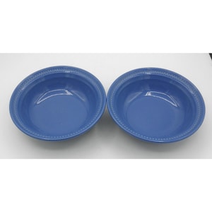 May include: Two round, medium-blue ceramic bowls with a smooth, glossy finish. Each bowl features a distinct, raised beaded texture along the inner rim, creating a decorative border. The bowls are identical in shape, color, and size.