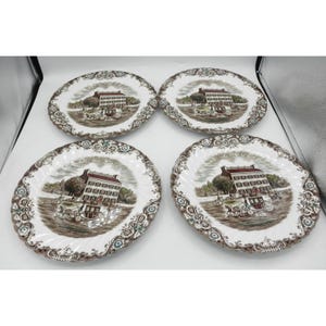May include: A set of four white ceramic plates featuring a brown transferware design. Each plate displays a multi-story building with a horse-drawn carriage in the foreground, surrounded by a decorative floral and scroll border in brown tones.