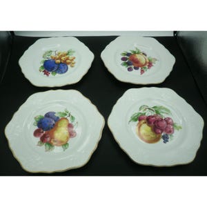 May include: Four white porcelain plates with scalloped edges and gold trim. Each plate features a different fruit design: grapes, peaches, plums, and cherries. The fruit illustrations are in vibrant colors.
