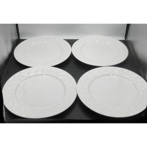May include: Four white ceramic plates with a textured, geometric pattern around the rim. The plates are round and have a smooth, glossy surface in the center. The plates are arranged in a square formation.