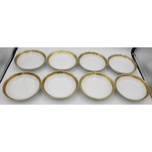 May include: Eight white oval-shaped bowls with a gold-colored decorative rim. The bowls are arranged in two rows of four, showcasing a classic design. The gold rim adds a touch of elegance to the tableware.
