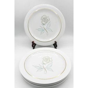 May include: White ceramic plates with a gold rim and a gold and teal rose design. The plates are stacked and displayed on a dark brown stand. The plates are a vintage style.