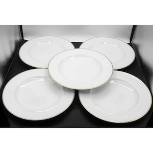 May include: A set of five round white ceramic dinner plates arranged in a cluster. Each plate features a smooth, glossy finish and a thin, metallic gold rim along the outer edge. The plates are plain with no additional patterns or designs.