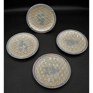 May include: Four decorative plates with a woven texture and a floral design in the center. The plates have a light blue border and a brown dotted trim. The plates are round and appear to be made of ceramic.