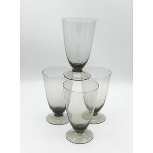 May include: Four gray-tinted, stemmed drinking glasses. One glass is stacked on top of the other three. The glasses have a classic, elegant shape with a wide bowl and a sturdy base. The glasses are made of clear glass.