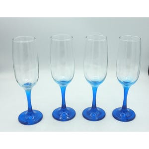 May include: Four clear champagne flutes with vibrant blue stems and bases. The glasses have a classic, elegant design, perfect for celebratory occasions. The blue color adds a touch of sophistication to the glassware.