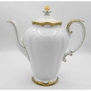 May include: White porcelain teapot with a gold-colored trim and accents. The teapot has a curved spout, a curved handle, and a lid with a gold finial. The base of the teapot also has gold trim. The teapot is a classic design.