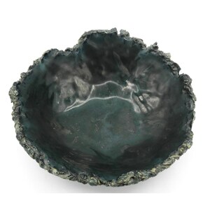 May include: A handcrafted, dark teal-colored ceramic bowl with a textured, organic rim. The bowl's interior has a glossy finish, and the rim has a rough, uneven edge. The overall design suggests a natural, earthy aesthetic, suitable for decorative or functional use.