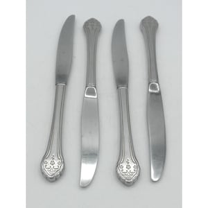 May include: Four silver-toned stainless steel dinner knives arranged vertically. Each knife features a smooth, curved blade and a handle decorated with an embossed floral pattern at the base and a central vertical line detail along the stem.