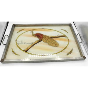 May include: Rectangular serving tray with a metal frame and handles. The tray features a peacock design in the center, with a brown branch and a yellow and orange background. The peacock has red, brown, and yellow feathers.