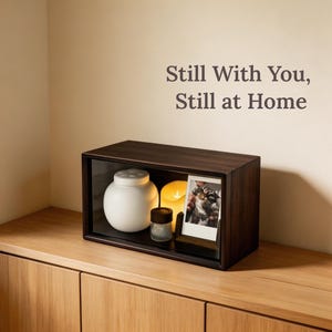 Home memorial display for a beloved cat or dog with walnut wood urn box, soft candle light, pet photo, and keepsake items arranged on a shelf.
