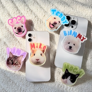 May include: Five circular phone grips featuring custom pet portraits and names. The grips display a French bulldog named Coco, a Labrador named Teddy, a guinea pig named Milo, a cat named Luna, and a cat named Mochi, each with colourful lettering.