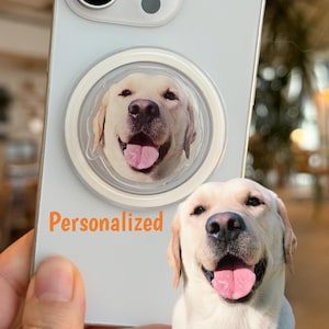 May include: A light-colored phone case with a personalized image of a smiling Labrador Retriever dog. The word "Personalized" is printed in orange. A matching pop socket with the dog's face is attached to the phone.