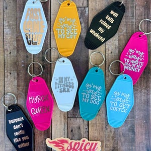 May include: A collection of colorful keychains with various phrases, including "Fast Lane Club," "On my way to see my cat," and "Wall balls ruined my weekend." The keychains are in various colors, such as black, pink, and blue.