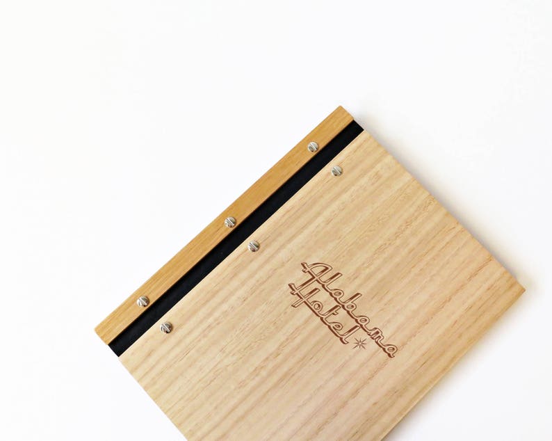 Timber compendium rests on a white background. The folder is made of Tasmanian oak, with black binding and 6 nickel screws. The cover is engraved with the logo of boutique hotel.