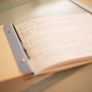 A wedding guestbook is open on a table top, showing a white paper page that has been filled with written messages.