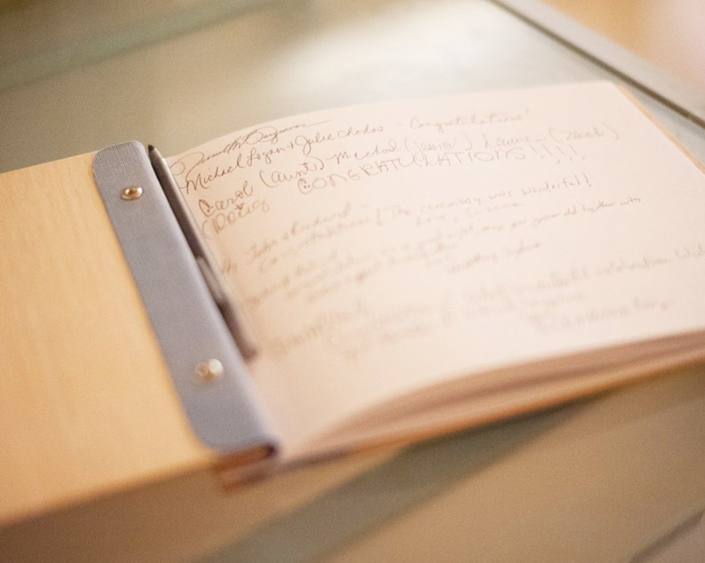 A wedding guestbook is open on a table top, showing a white paper page that has been filled with written messages.