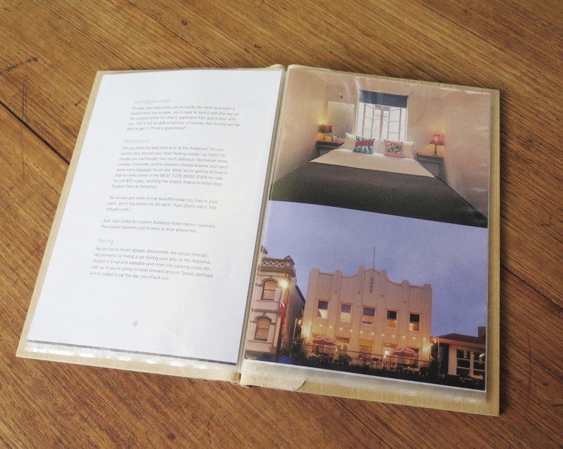 A timber A5 size compendium lies open on a wood table. The plastic sleeves display images of a boutique hotel, and a list of house rules.