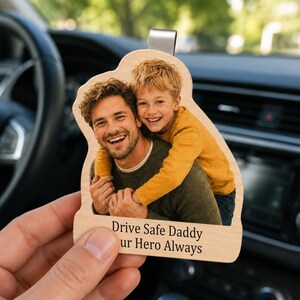 May include: Wooden car charm with a photo of a smiling father and son. The charm has a metal clip for hanging and the text "Drive Safe Daddy ur Hero Always" is printed in black.