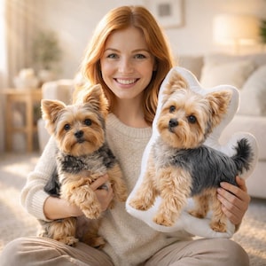 May include: A woman holding a live Yorkshire Terrier dog and a dog-shaped pillow. The dog is tan, black, and gray. The pillow is white with a printed image of a Yorkshire Terrier. The woman is smiling and has red hair.