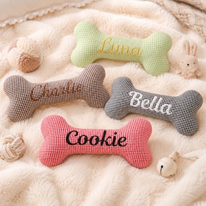 Peut inclure: Plusieurs jouets pour chiens, dont des os en peluche personnalis&eacute;s avec les noms "Luna", "Charlie", "Bella" et "Cookie" brod&eacute;s. Les os sont de diff&eacute;rentes couleurs et motifs, accompagn&eacute;s d'autres jouets et d'un petit lapin en peluche.
