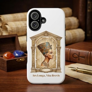 May include: A white smartphone case featuring a central illustration of Nefertiti in profile, framed by an ornate architectural archway. The text "NEFERTITI 1353 BC" appears above the portrait, and "Ars Longa, Vita Brevis" is printed at the bottom.