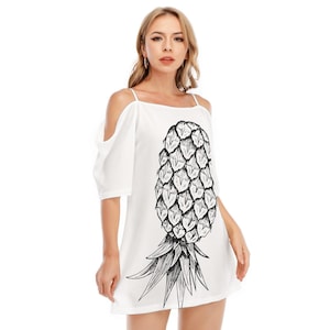 May include: White off-the-shoulder dress featuring a large black and white pineapple graphic. The dress has a loose fit with short sleeves and thin spaghetti straps. The pineapple design is detailed with a textured pattern.