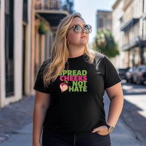 Peut inclure: T-shirt noir avec un graphique de pêche et le texte "Spread Cheeks Not Hate" en lettres vertes et roses.