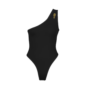 May include: A solid black one-shoulder bodysuit featuring a small, embroidered gold pineapple icon positioned near the top of the shoulder strap. The garment has a clean, minimalist design with visible stitching along the edges and a high-cut leg.