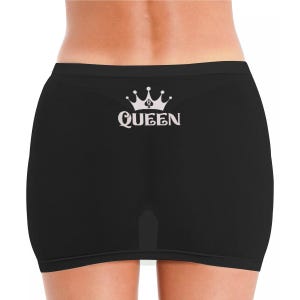 May include: Black underwear featuring a white graphic print on the back. The design consists of a stylized crown icon positioned above the word QUEEN in a decorative serif font. The garment has a solid black color and a smooth, seamless appearance.